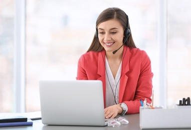 Photo of Young woman talking on phone through headset at workplace