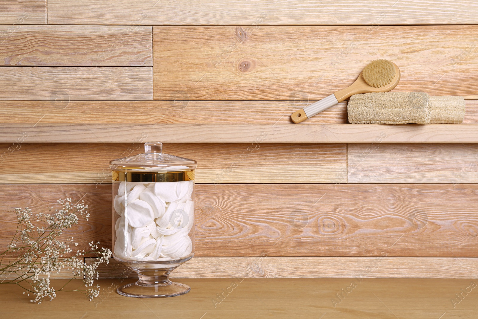 Photo of Composition of glass jar with cotton pads on table near wooden wall. Space for text