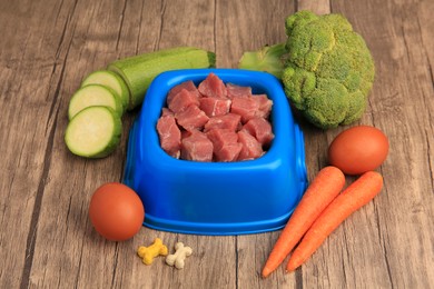 Photo of Raw meat in pet bowl, products and vitamins on wooden background