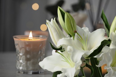 Image of Funeral. White lilies and burning candle indoors, bokeh effect