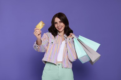 Photo of Beautiful young woman with paper shopping bags and credit card on purple background