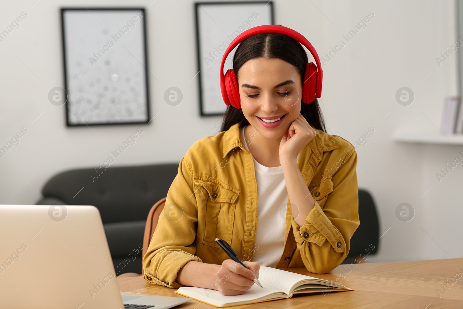 Photo of Online translation course. Student in headphones writing near laptop at home