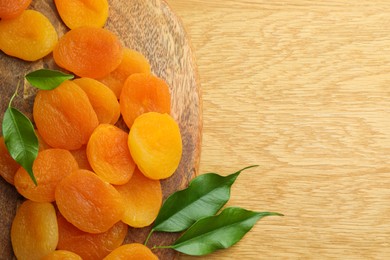 Photo of Tasty apricots and green leaves on wooden table, top view with space for text. Dried fruits