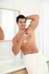 Photo of Handsome young man applying deodorant in bathroom