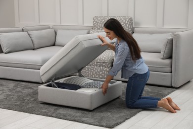 Photo of Woman opening modular sofa section with storage in living room