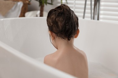 Photo of Cute little girl washing hair with shampoo in bathroom