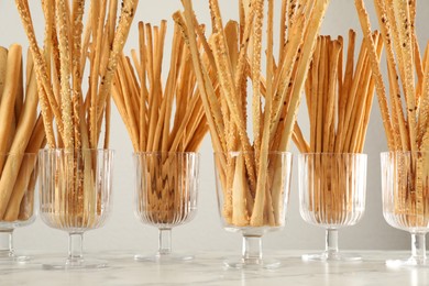 Photo of Delicious grissini sticks served in glasses on white marble table
