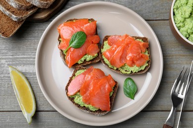 Delicious sandwiches with salmon and avocado served on grey wooden table, flat lay