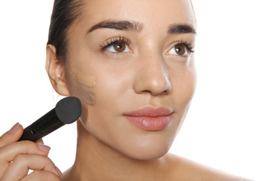 Photo of Young woman applying foundation on her face against white background
