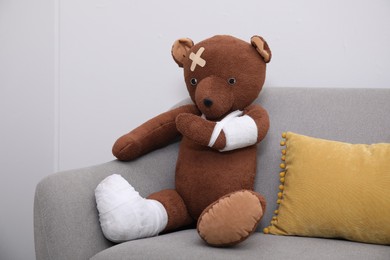 Photo of Toy bear with bandages sitting on sofa near light wall