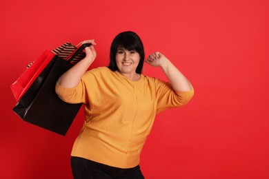 Beautiful overweight mature woman with shopping bags on red background