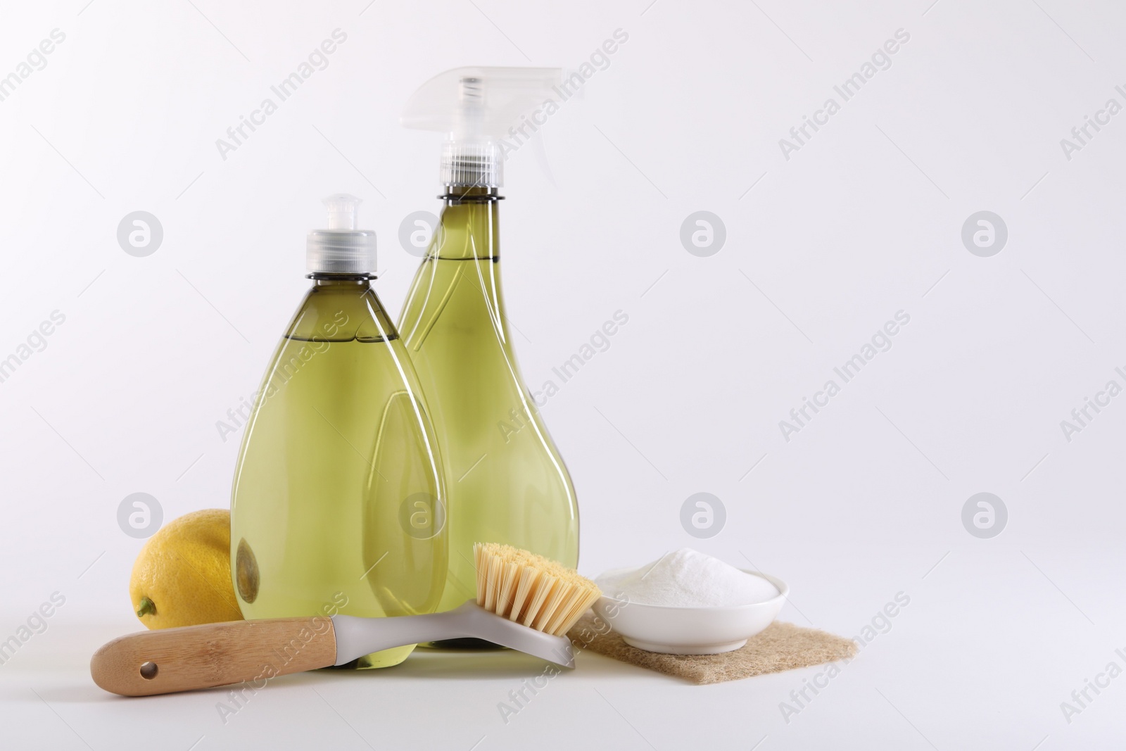 Photo of Bottles of cleaning product, brush, baking soda and lemon on white background