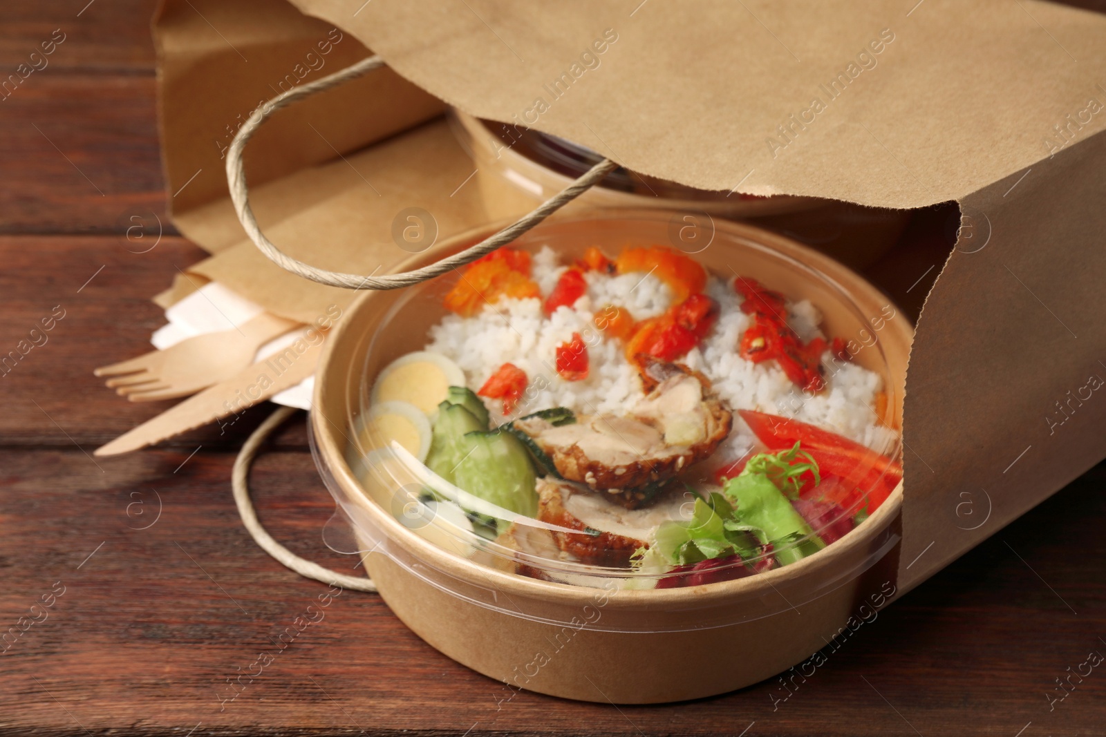 Photo of Tasty food in container with knife and fork on wooden table, closeup