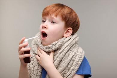 Little boy with scarf using throat spray on grey background