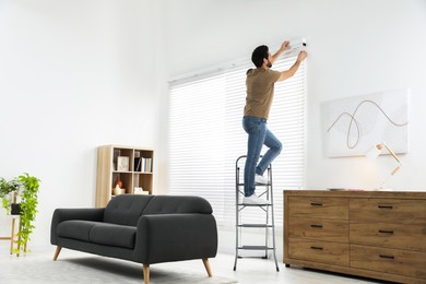 Photo of Man on metal folding ladder installing blinds at home. Space for text