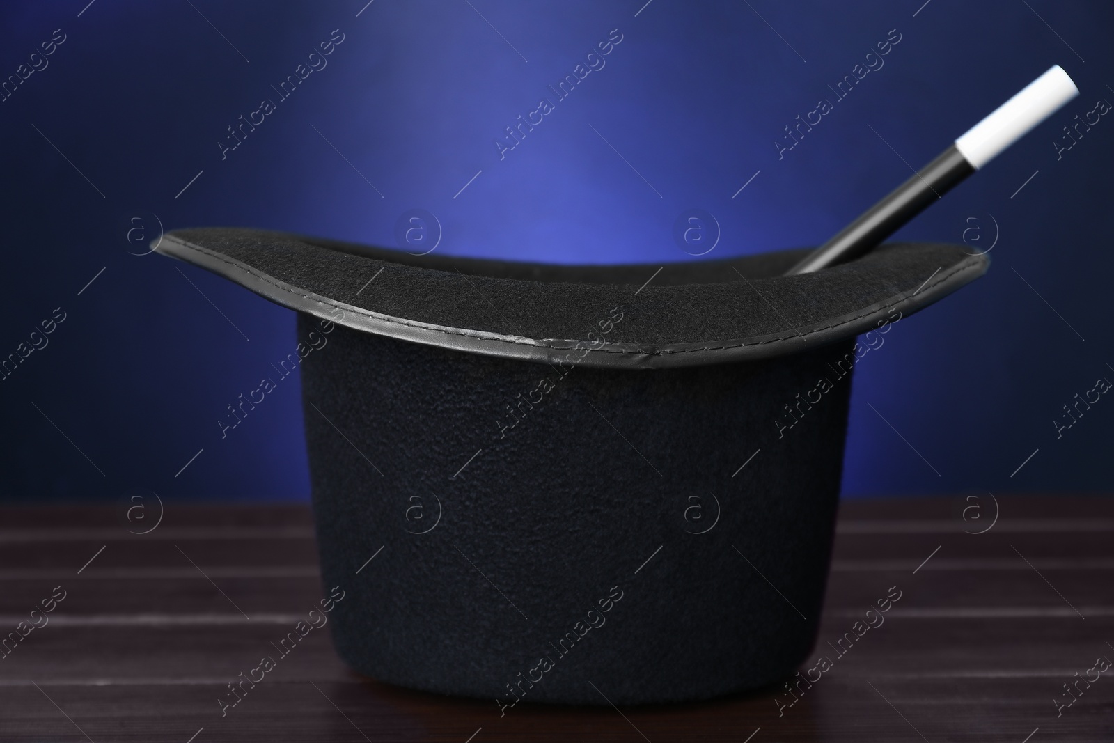 Photo of Black top hat and wand on wooden table against color background, closeup. Magician equipment