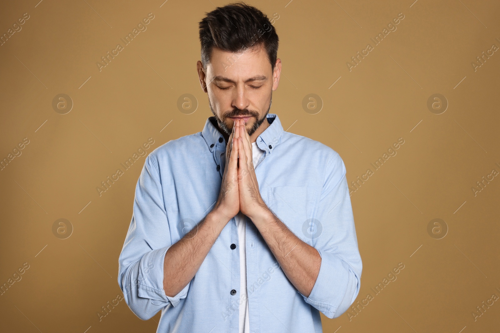 Photo of Man with clasped hands praying on beige background