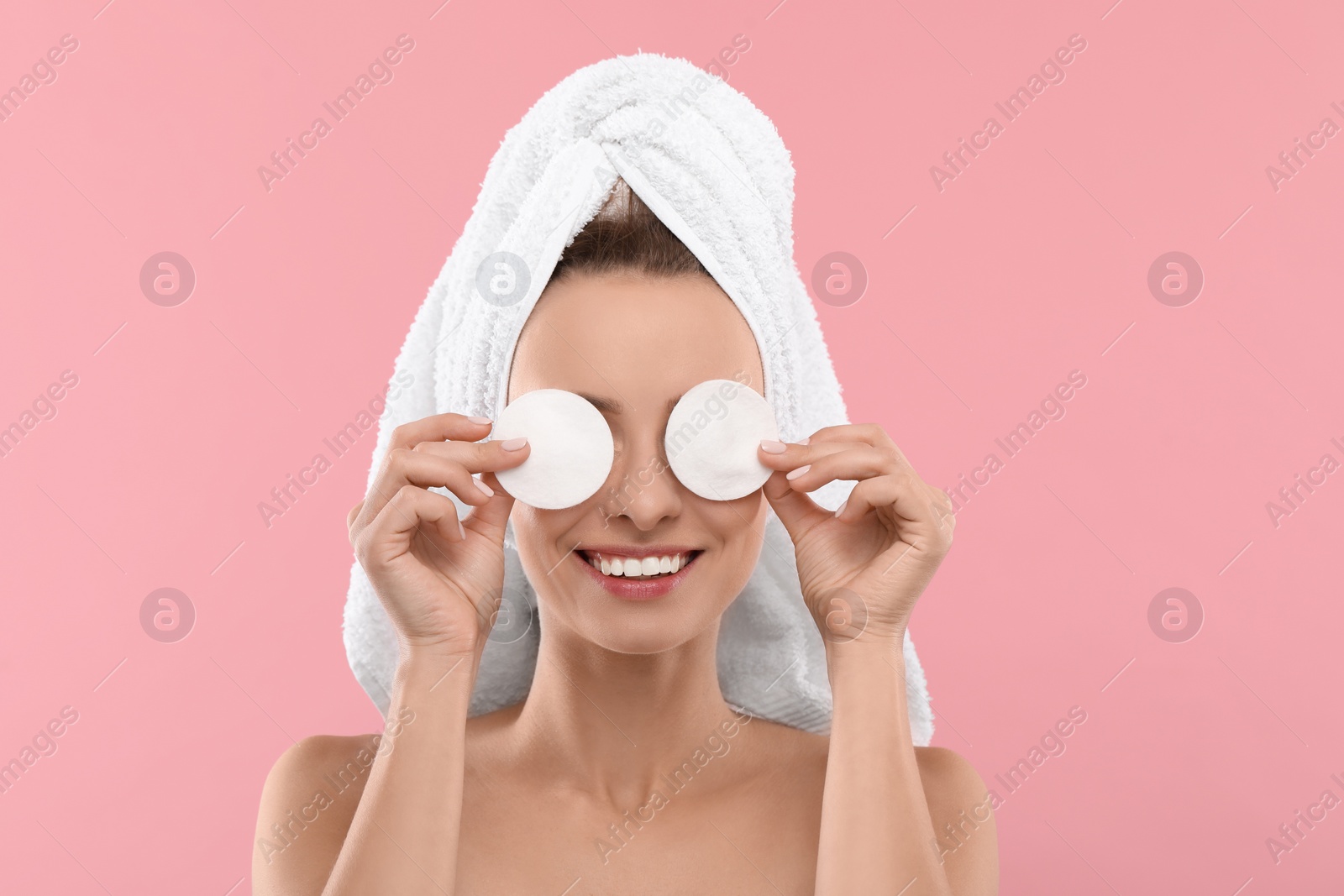 Photo of Smiling woman removing makeup with cotton pads on pink background