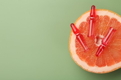 Skincare ampoules with vitamin C and half of grapefruit on light green background, top view. Space for text