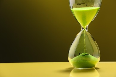 Photo of Hourglass with light green flowing sand on table against color background. Space for text