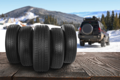 Snow tires on wooden surface and winter landscape with car