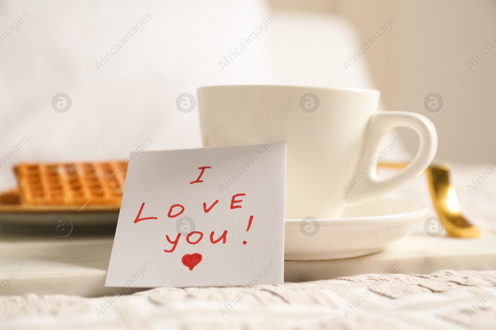 Photo of Paper note I Love You near cup of morning drink and waffles on bed. Romantic breakfast