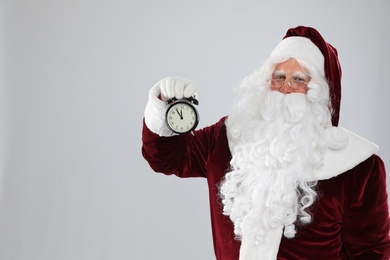 Photo of Santa Claus holding alarm clock on light grey background, space for text. Christmas countdown
