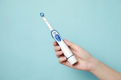 Woman holding electric toothbrush on light blue background, closeup