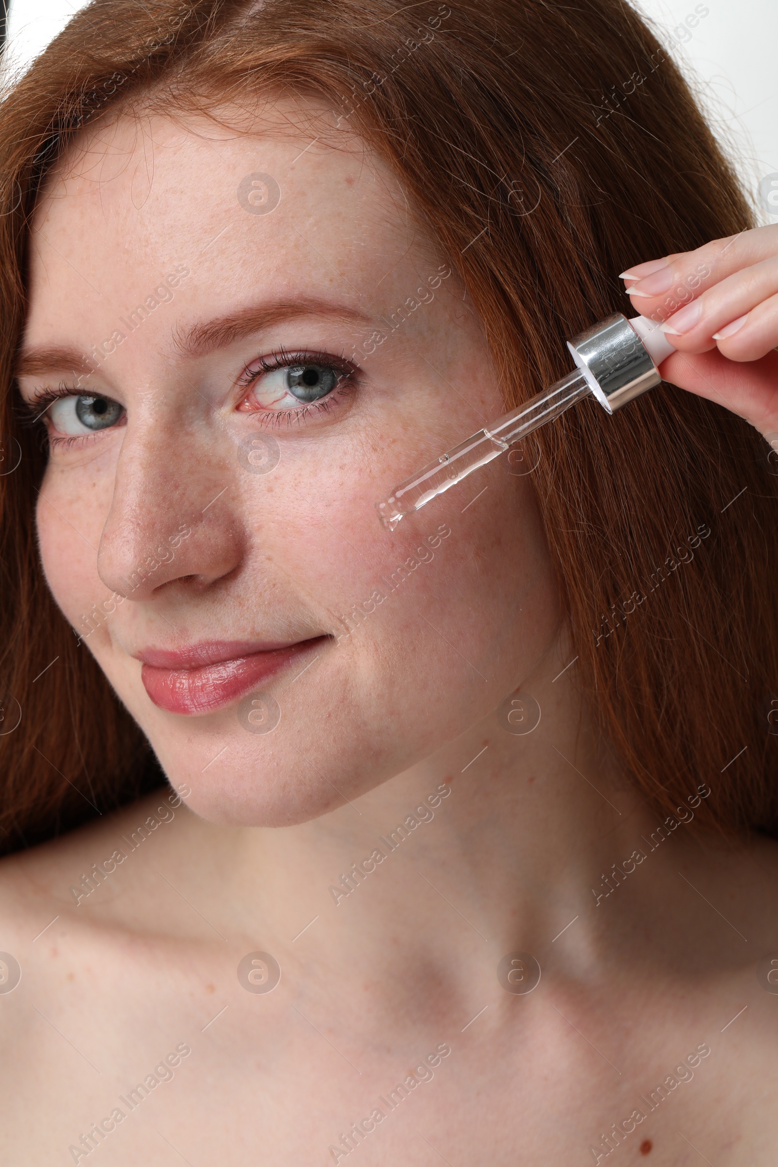 Photo of Beautiful woman with freckles applying cosmetic serum onto her face, closeup