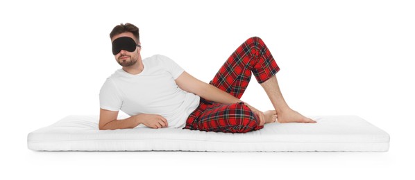 Photo of Man wearing sleeping mask on soft mattress against white background
