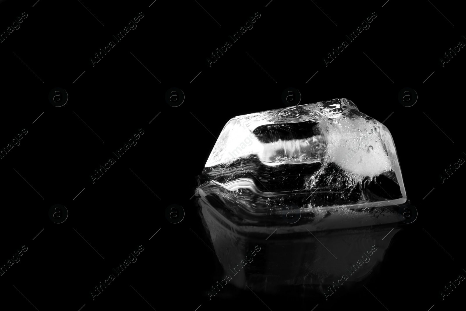 Photo of Ice cube on black mirror surface. Space for text