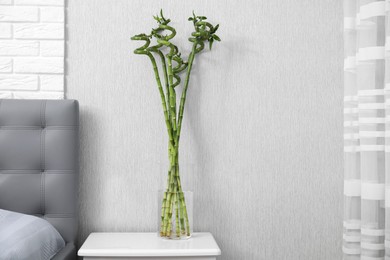 Vase with beautiful green bamboo stems on white bedside table indoors