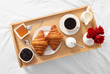 Photo of Tasty breakfast served in bed. Fresh croissants, coffee, honey and jam on wooden tray