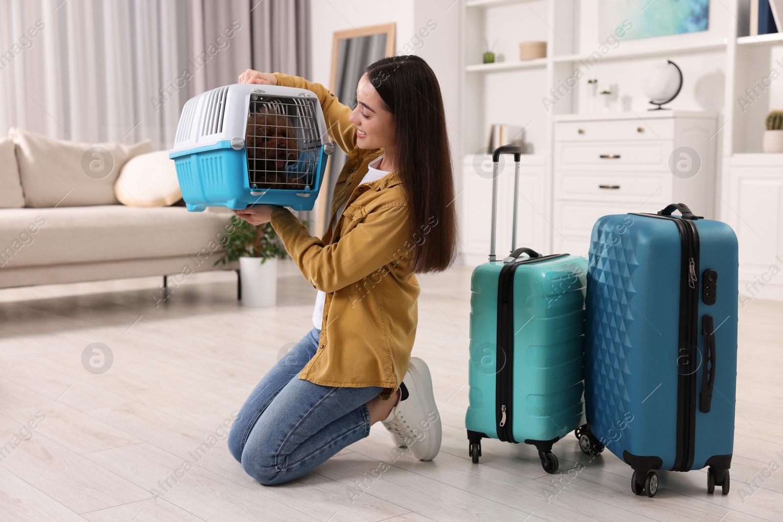 Photo of Travelling with pet. Smiling woman looking at carrier with her dog indoors