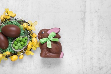 Photo of Flat lay composition with chocolate Easter bunny, eggs and candies on white textured table. Space for text