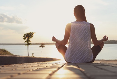 Photo of Young woman meditating near river in morning, back view. Space for text