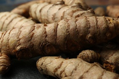 Many raw turmeric roots on black textured table, closeup