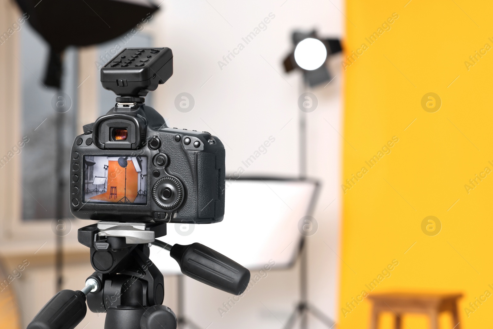 Photo of Tripod with camera, bar stool and professional lighting equipment in modern photo studio, focus on screen. Space for text