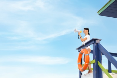 Photo of Female lifeguard with megaphone on watch tower against blue sky