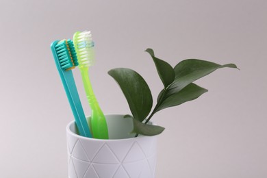 Photo of Colorful plastic toothbrushes and plant twig in container on light background, closeup