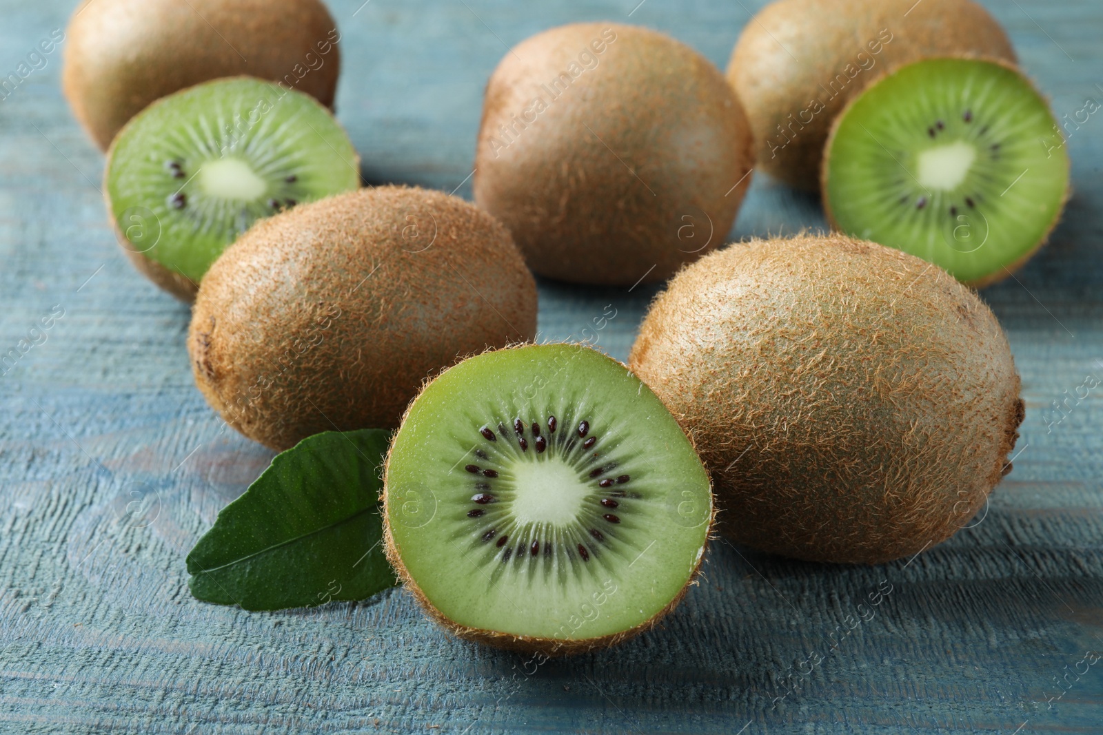 Photo of Cut and whole fresh ripe kiwis on light blue wooden table, closeup