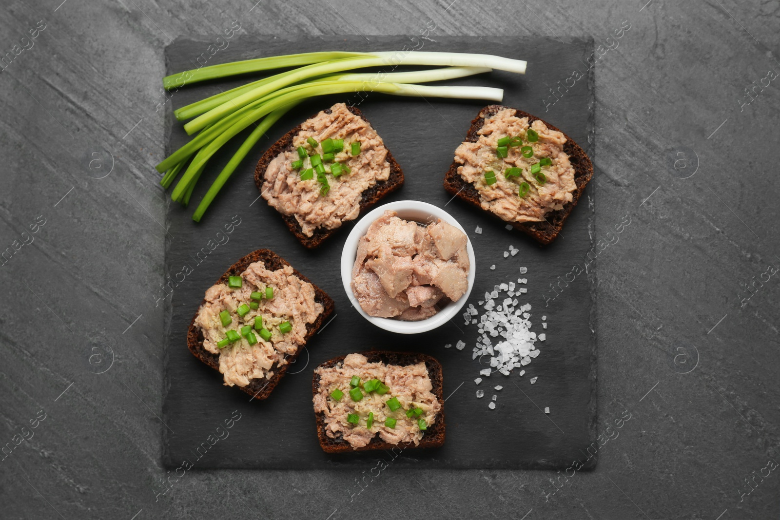 Photo of Tasty sandwiches with cod liver, salt and green onion on grey table, top view