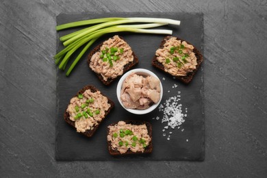 Photo of Tasty sandwiches with cod liver, salt and green onion on grey table, top view