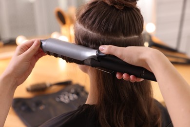 Photo of Hairdresser curling woman's hair with iron in salon, closeup