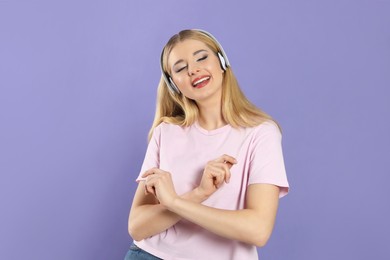 Photo of Happy woman in headphones enjoying music and dancing on violet background