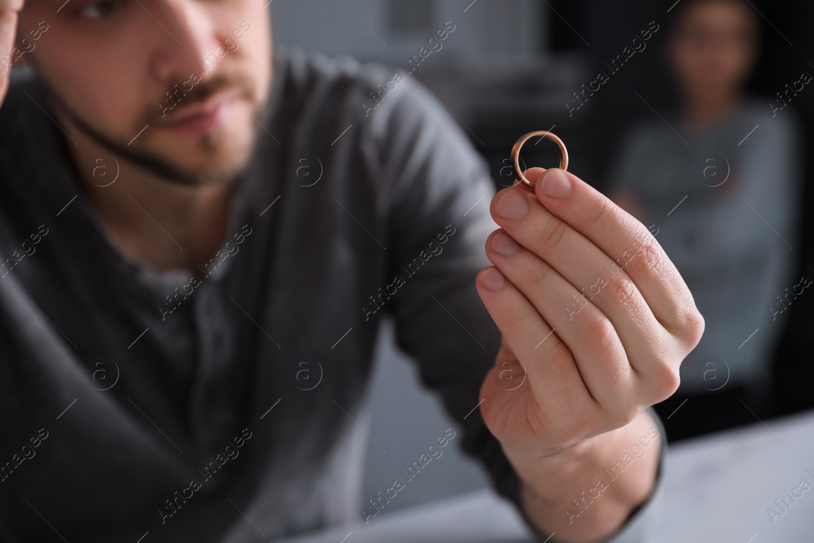 Photo of Sad man holding wedding ring at table indoors, closeup. Couple on verge of divorce