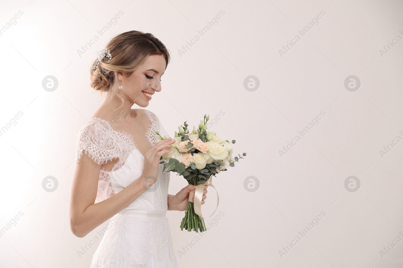 Photo of Young bride with elegant hairstyle holding wedding bouquet on white background