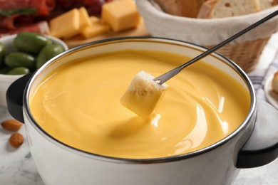Photo of Dipping piece of bread into tasty cheese fondue at white table, closeup