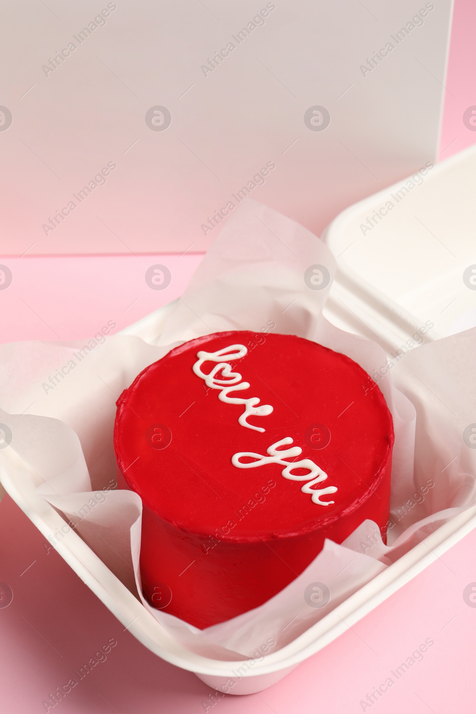 Photo of Tasty bento cake with Love You inscription in takeaway box on pink table