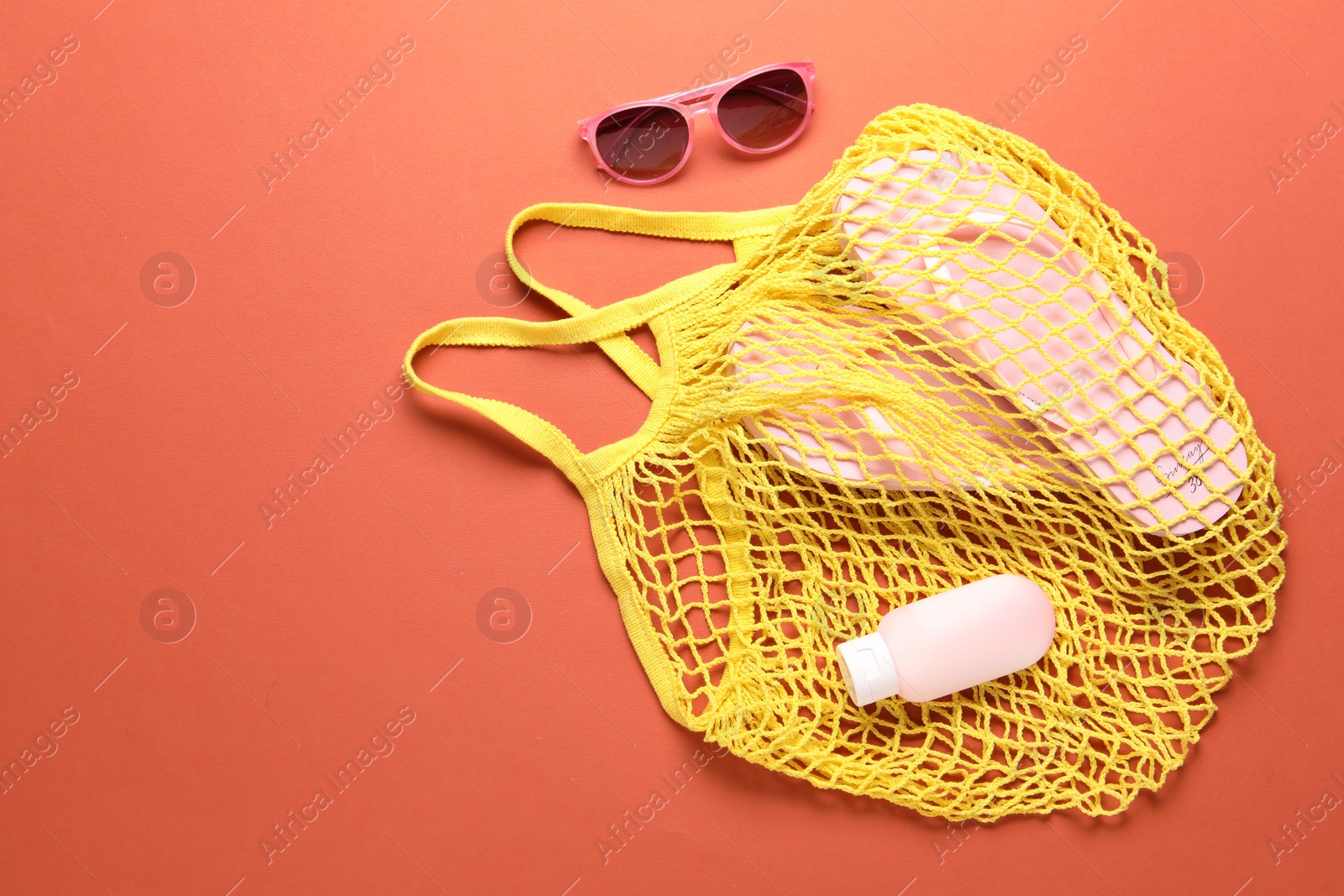 Photo of String bag, sunglasses, cosmetic product and slippers on coral background, top view. Space for text